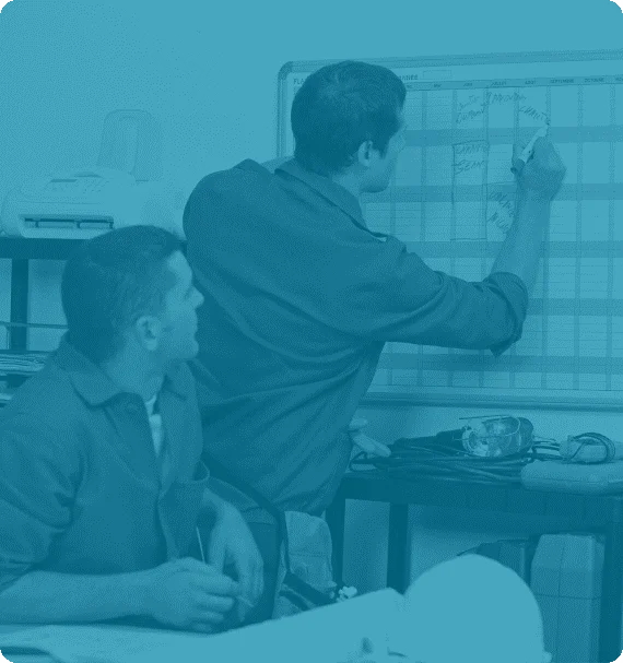 Two maintenance professionals reviewing and updating a scheduling board—illustration from Reliability Academy’s PS100 Planning & Scheduling online training course